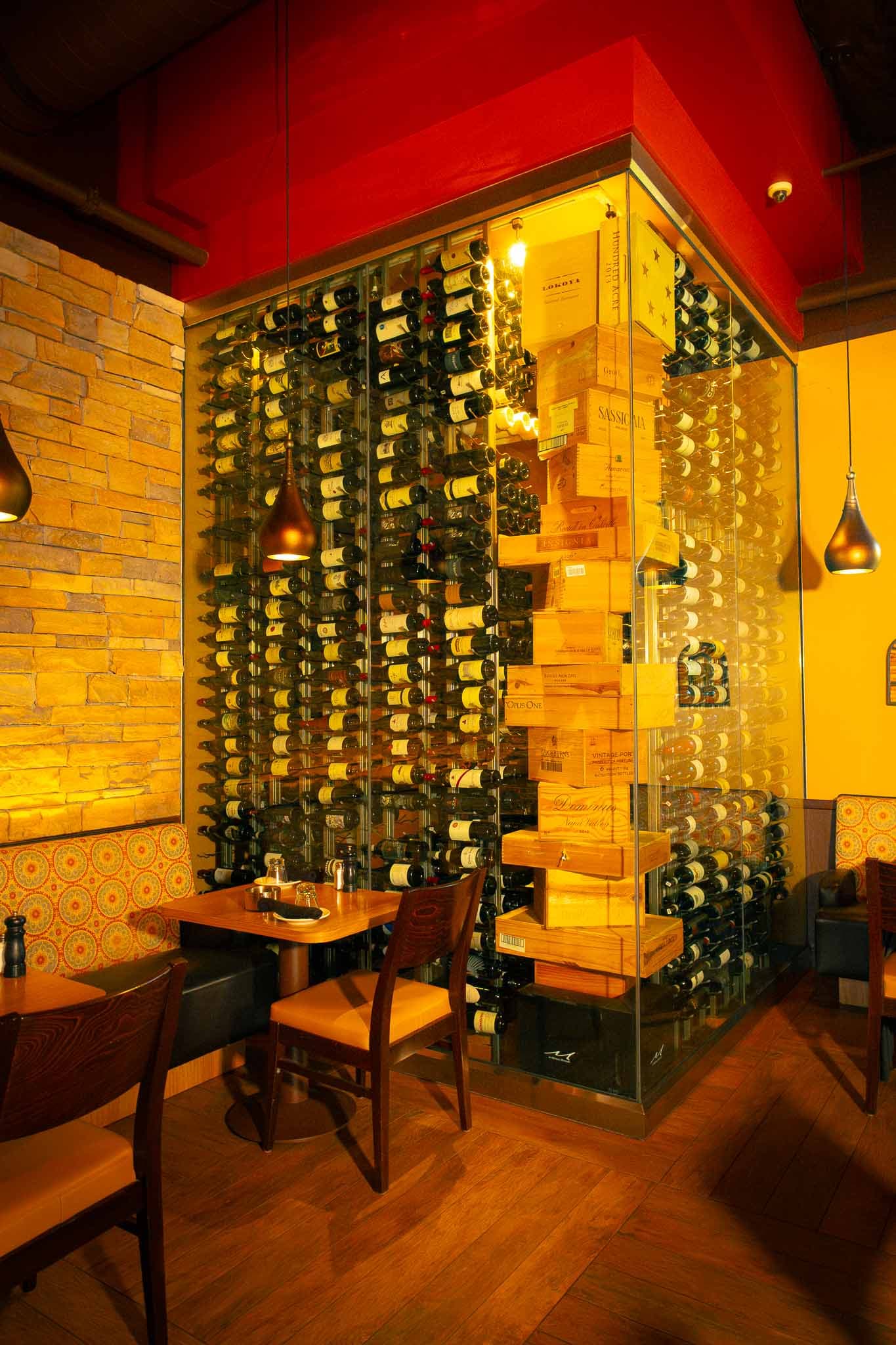 Yanni's private cellar in San Diego — a tall wall of bottle racks glowing under amber light, framed by a dramatic red ceiling